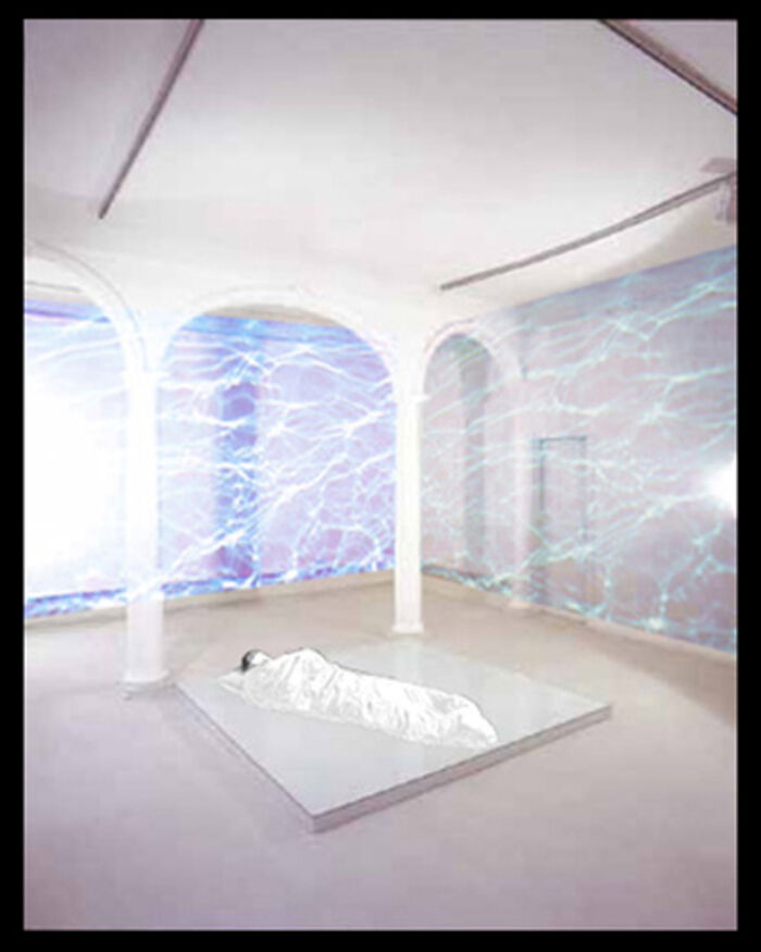 Gallery installation with white arches and electric-blue projected patterns on the walls, a shrouded figure on the floor.