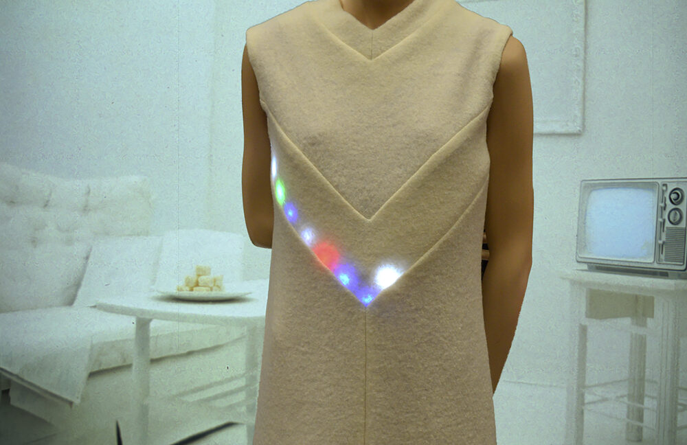 A person wearing a pale sleeveless dress with a row of embedded colourful LED lights glowing along the neckline.