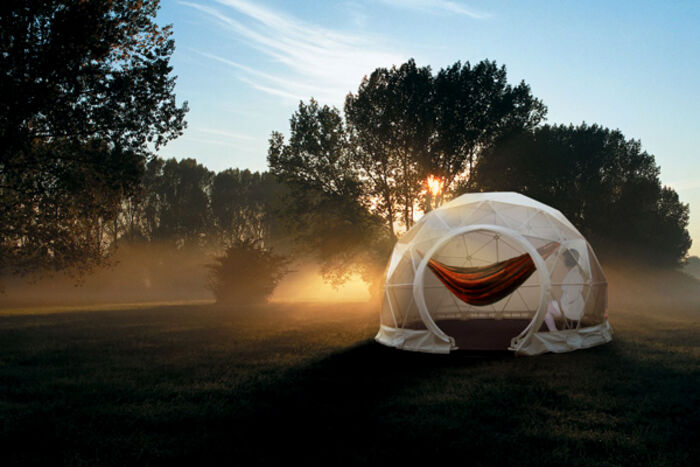 A geodesic dome structure in a misty field at dawn, warm light glowing from within.